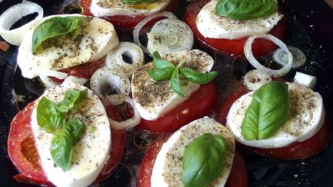 Frische Tomatenscheiben mit Mozzarella und Basilikum werden in Olivenöl gewürzt, ideal für einen gesunden Tipp zum Abnehmen.