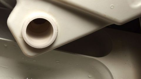 Weniger Wasser beim Waschen mit der Waschmaschine verbrauchen mit Kondenstrocknerwasser. Ein Wassertank eines Kondenstrockners gibt Wasser ab, das zum Waschen verwendet werden kann, eingebettet in einer Haushaltsumgebung.