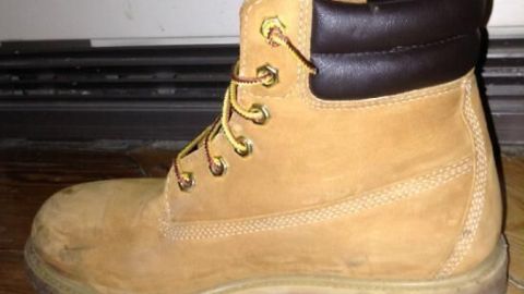 Ein einfacher Tipp, um deine Timberlands sauber zu halten: Nutze einen Radiergummi, um Flecken und Schmutz auf den robusten Lederstiefeln zu entfernen. Pflege leicht gemacht für ein gepflegtes Aussehen deiner Lieblingsschuhe. Ein einzelner Timberland-Stiefel steht auf einem Holzboden vor einer weißen Wand, deutlich sichtbar im Profil.