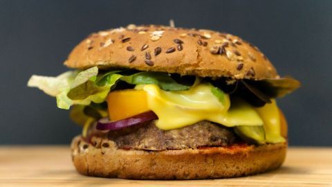Ein vegetarischer Burger mit einem Pattie, frischem Gemüse und geschmolzenem Käse wird appetitlich auf einem Holzbrett präsentiert.