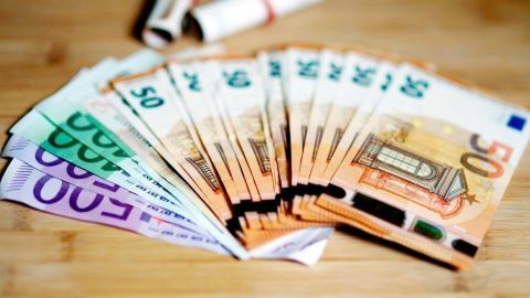 Sichere dein Bargeld clever: Der Artikel erklärt, wie du Banknoten geschickt in ungenutzten Haushaltsgegenständen versteckst. Das Bild zeigt, dass ordentlich gefaltetes Geld schnell und unauffällig verstaut werden kann. Euro-Geldscheine liegen fächerförmig auf einem Holztisch, daneben zwei aufgerollte Geldbündel als mögliches Geldversteck.