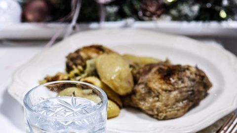 Ein Glas Wasser steht neben einem Teller mit Hähnchengerichten und Beilagen, dekoriert mit festlicher Tischdekoration.
