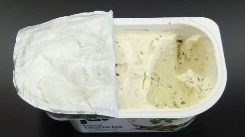 Ein geöffneter Behälter mit angefangenen Frischkäse steht auf einem dunklen Hintergrund, bereit für Resteverwertung.