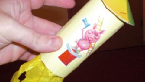 Eine handgefertigte Deko-Rakete wird mit einem fröhlichen Schweinchen-Motiv in einem Raum gehalten, umgeben von Bastelmaterial.