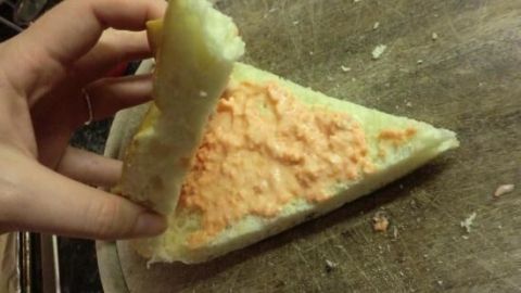 Ein halb aufgeklapptes Pitabrot wird mit einer orangefarbenen Füllung gehalten, während es auf einem Holzbrett liegt.