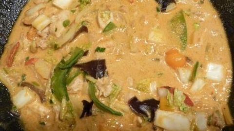 Ein thailändischer Eintopf mit buntem Gemüse und einer cremigen, würzigen Sauce in einer dunklen Schale.