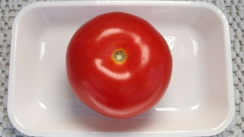 Stielansatz von Tomaten sind ganz leicht und schnell zu entfernen, mit einer Spritztülle aus Metall. Eine rote Tomate liegt in einer weißen Schale und wartet darauf, den Stielansatz entfernt zu werden.