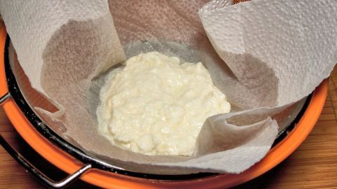 In einem Sieb aus Kunststoff, ausgekleidet mit Küchenpapier, ruht dicker Magerjoghurt, der auf seine Sahne-Konsistenz wartet.