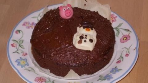 Eine kleine Erdnuss-Schokoladen-Torte steht auf einem blumengeschmückten Teller, dekoriert mit bunten Figuren.