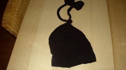 Eine schwarze Perücke liegt auf einem Tisch und ist mit Bändern zum Sichern versehen, ideal, um ein Verrutschen zu verhindern.