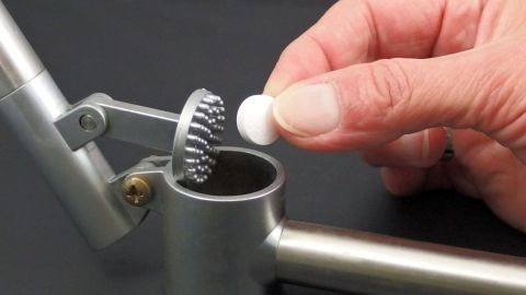 Tabletten mit der Knoblauchpresse zerkleinern - funktioniert prima! Eine Hand hält eine Tablette, während sie sie in einen Tablettenteiler legt, um sie zu zerkleinern.