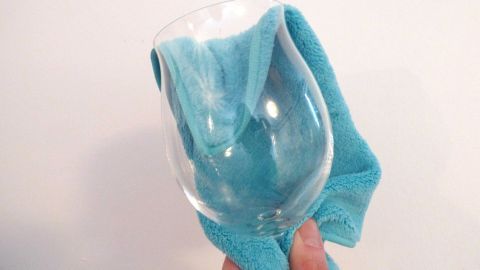 Hand trocknet Glas mit blauem Tuch, Nahaufnahme, vor weißem Hintergrund.