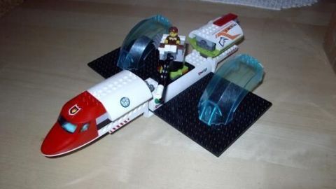 Ein rotes und weißes Spielzeugflugzeug mit einem Piloten, landend auf einer dunklen Unterlage, umgeben von Weihnachtsdekoration.