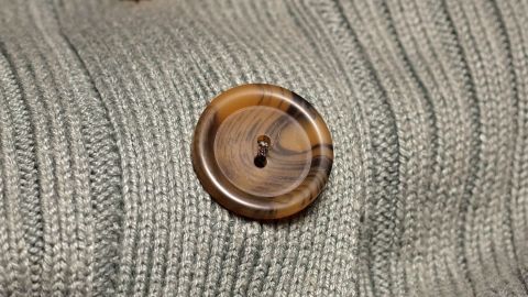 Ein Kleidungsstück mit auffälligen, hässlichen Knöpfen liegt auf einer gestrickten Oberfläche in sanften Farben.