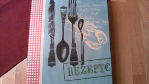 Ein originelles Kochbuch liegt auf einem Holztisch, verziert mit Besteckillustrationen und dem Wort "Rezepte" auf dem Cover.