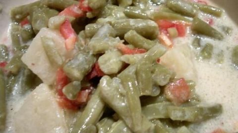 Ein Bohnensalat mit grünen Bohnen und Paprika liegt in einer cremigen Sauce, serviert auf einem Teller.