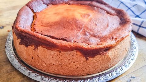 Ein Quarkkuchen steht auf einem silbernen Teller, gebräunt und frisch gebacken, auf einem rustikalen Holztisch.