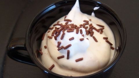 Eine dunkle Tasse enthält cremigen Quark mit einer schaumigen Schicht und ist mit Schokoladenstreuseln garniert.