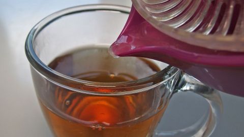 Ein Teekanne gießt heißen Tee in eine Tasse, die als Hausmittel bei Erkältung dient. Der Hintergrund ist einfach und hell.