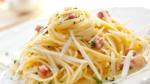 Spaghetti liegen auf einem Teller und sind mit Carbonara-Soße, Speck und Käse in einer hellen Umgebung angerichtet.