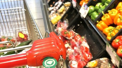 Der Einkaufswagen mit einem Chip am Schlüssel liegt bereit, während frisches Gemüse in den Regalen daneben steht.