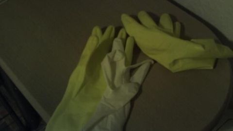 Zwei Handschuhe liegen auf einem Tisch: ein weißer Latexhandschuh unter einem grünen Gummihandschuh.