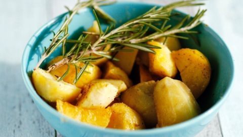 Kartoffeln liegen in einer blauen Schüssel und sind mit Rosmarin garniert, auf einem hellen Holzuntergrund angerichtet.