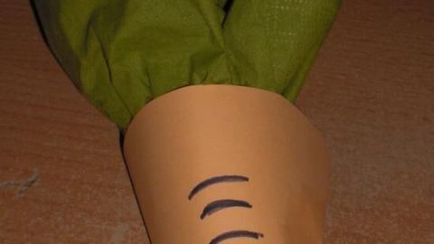 Ein orangefarbenes Serviettenformat in Form einer Möhre hält grüne Serviettenblätter, ideal für Ostern.