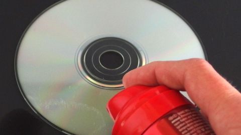 Ein Hand hält eine rote Sprühdose über eine glänzende CD, während Haarspray auf die CD aufsprüht.
