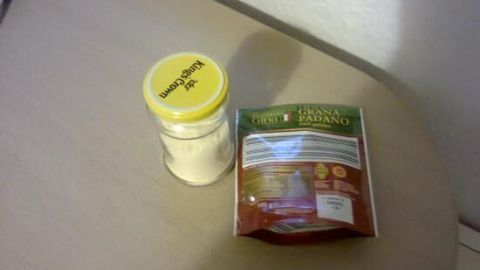 Ein Schraubglas mit Parmesan steht auf einem Tisch neben einer Verpackung, bereit zum Umfüllen für die Aufbewahrung.