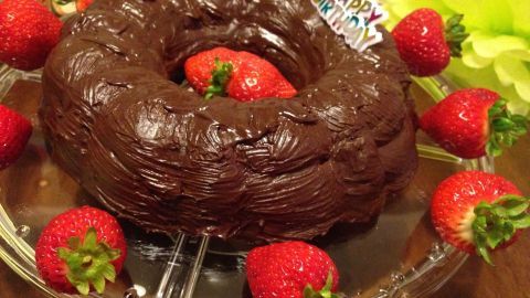 Ein schokoladiger Schokokuchen steht auf einer Glasplatte, umgeben von frischen Erdbeeren und einem Geburtstagsgruß.