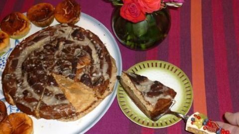 Ein Zitrus-Mandel-Kuchen liegt auf einem Teller, während ein Stück auf einen kleinen Teller serviert wird, umgeben von Gebäcken und einer Blumenvase.