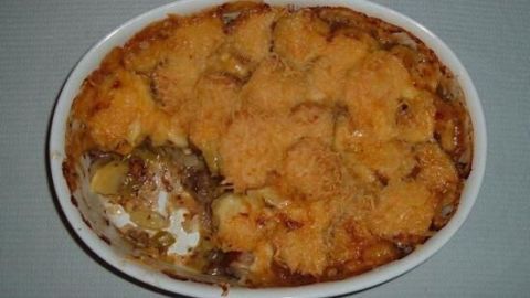 Ein goldbrauner Kartoffelauflauf mit Bratwurst und Porree ist in einer weißen Auflaufform angerichtet und duftet köstlich.
