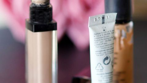 Drei Concealer stehen auf einem Tisch vor rosa Blumen. Der flüssige Concealer ist geöffnet, bereit zur Anwendung.