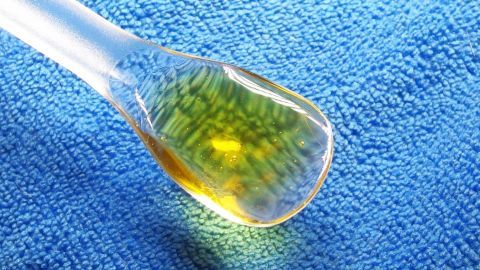 Eine Pipette mit gelblichem Öl liegt auf einem blauen Tuch und könnte gegen Juckreiz bei Neurodermitis eingesetzt werden.