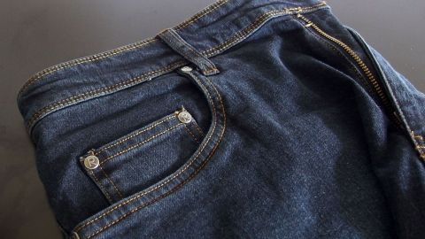 Um in dunklen Jeans die Farbe lange zu erhalten, kann man diese mit Essig vorbehandeln. Dunkle Jeans liegen ordentlich gefaltet auf einer schwarzen Oberfläche, bereit für die Pflege, um die Farbe zu erhalten.