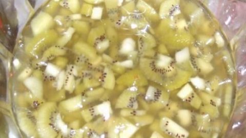 Eine Schüssel Kiwi-Bowle gefüllt mit geschnittenen Kiwi-Stücken in klarer Flüssigkeit, glänzend im Licht.