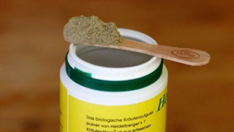 Ein Holzspatel steht auf einem geöffneten Behälter mit Gewürzpulver, das auf einem Holztisch platziert ist.