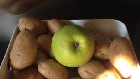 Eine Schüssel mit Kartoffeln, in der ein grüner Apfel in der Mitte steht, zeigt frische Lebensmittel in einer modernen Küche.