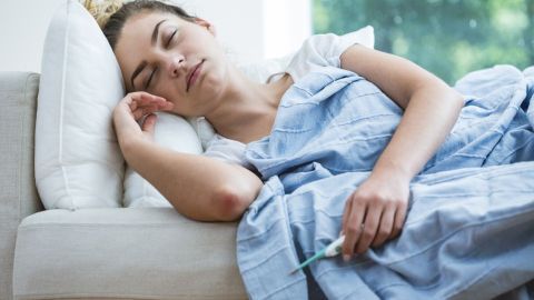 Eine schlafende Frau liegt auf einer Couch, umhüllt von einer Decke, und kämpft gegen ihre verstopfte Nase.