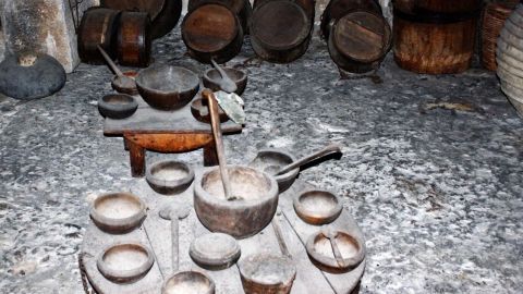 Holzgeschirr und Töpfe stehen auf einem Tisch in einer rustikalen Umgebung, die traditionelles Kochen simuliert.