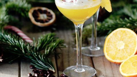 Ein Cocktailglas mit Apfelsinenlikör und Kaffee steht auf einem Holztisch, umgeben von grünen Zweigen und Orangenscheiben.