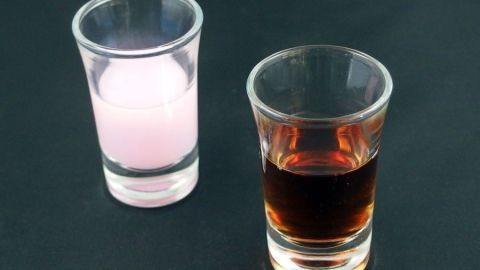 Ein Glas mit roter Flüssigkeit steht neben einem Glas mit rosa Flüssigkeit auf einem dunklen Tisch.