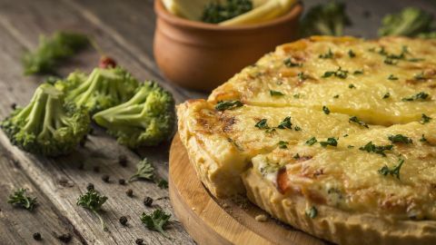Eine herzhafte Torte liegt auf einem Holzbrett, während frisches Gemüse und Kräuter die rustikale Umgebung ergänzen.