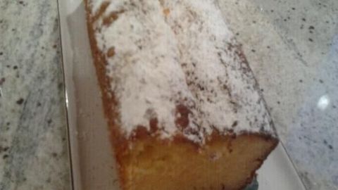 Ein frisch gebackener Orangenkuchen liegt auf einem eleganten Teller, bestäubt mit Puderzucker in einer hellen Küche.