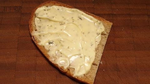 Ein Stück Brot ist mit Remoulade bestrichen und liegt auf einer Holzoberfläche, umgeben von einer rustikalen Atmosphäre.