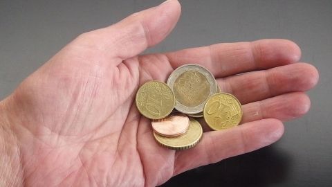 Eine Hand hält Münzen, während das Wechselgeld sofort nachgezählt wird. Der dunkle Hintergrund lenkt den Fokus auf die Geldstücke.