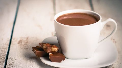 Eine weiße Tasse mit heißer Schokolade steht auf einem Unterteller, umgeben von hellen Holzbrettern.