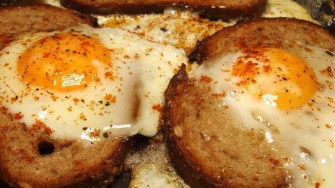 Gebratenes Brot mit Ei liegt in einer Pfanne, während das Ei brät und die Ränder goldbraun sind.