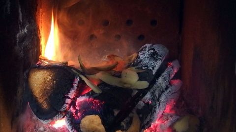 Ein Kamin brennt mit glühenden Kohlen und Holzscheiten, umgeben von den Mauern des Schornsteins.